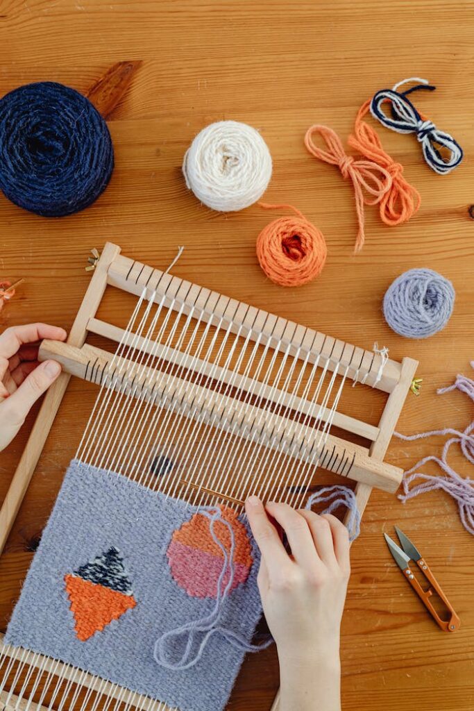 A close-up of hands weaving colorful wool on a wooden loom, showcasing craftwork.